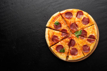 Pepperoni pizza, tomatoes and parsley. Tasty pepperoni pizza on black stone background. Overhead view of italian pizza.