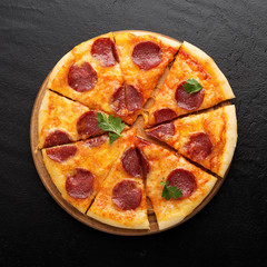 Pepperoni pizza, tomatoes and parsley. Tasty pepperoni pizza on black stone background. Overhead view of italian pizza.