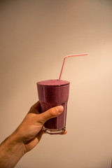 human hand holding a pink berry smoothie in front of plain white background