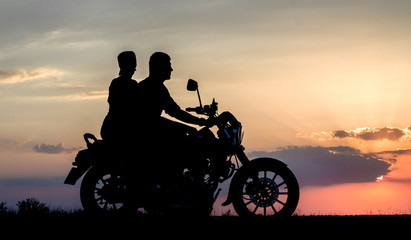 Naklejka na ściany i meble silhouette of a young couple man and woman on a motorcycle on sunset background