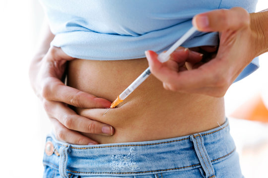 Female diabetes patient making subcutaneous insulin injection into her abdomen. Diabetes, health care and medical concept.