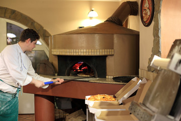 Piekarz wyjmuje pizze z pieca opalanego drewnem. - obrazy, fototapety, plakaty