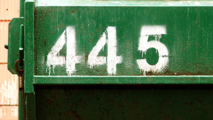 Number 445 painted with drips through stencil  on the side of metal container