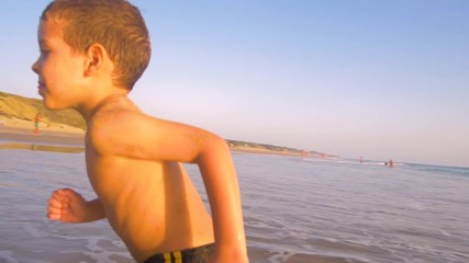 Slow motion - A child 3-5 years old running freely while the camera chase him and he laughs, in a sunny day in the beach 