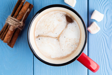red mug with hot cocoa or chocolate with cinnamon sticks and marshmallows