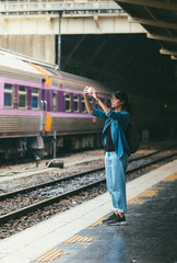 Asian woman traveler used smart phone take photos while wait and check train schedule on the platform of the railway station - travel and transportation concept