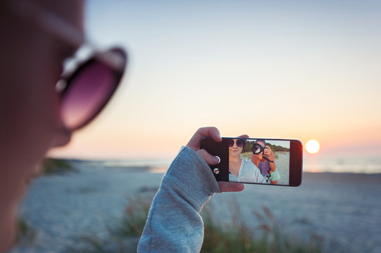 Girls taking selfie on spectacular sunset background with phone camera