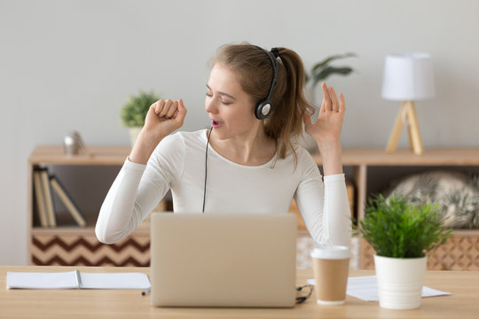 Joyful young millennial woman wearing headset with microphone sitting at the desk at home or office opposite computer enjoy music and singing. Student studying online e-learning or worker has a break