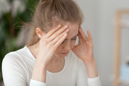 Close up portrait worried millennial young woman sitting in office or home. Upset female worker feels unhealthy has headache or eyestrain. Student girl received bad news or exam test failure concept