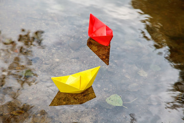 two multicolored paper boats floating on a stream