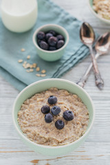 Oatmeal porridge bowl on the white wooden background.