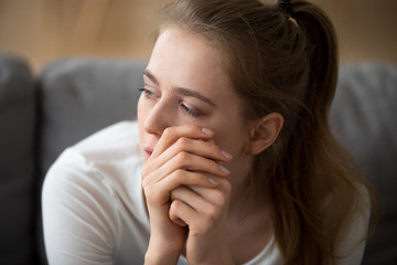 Close up portrait of sad woman thinking alone sitting on couch at home. Girl feels unhappy and...
