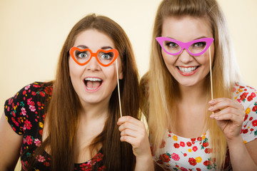 Two happy women holding fake eyeglasses on stick