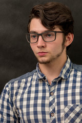 serious young man with glasses on black background.