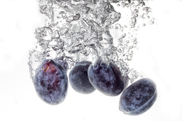 Plums falling into water, isolated on a white background