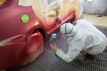 Repair and painting car car mechanic. Auto mechanic worker painting car in a paint chamber during repair work. Auto repairman plastering autobody bonnet.  - obrazy, fototapety, plakaty