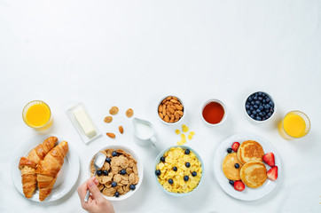 Breakfast table setting with flakes, juice, croissants, pancakes and fresh berries