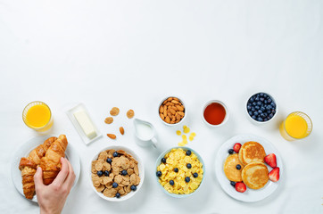 Breakfast table setting with flakes, juice, croissants, pancakes and fresh berries