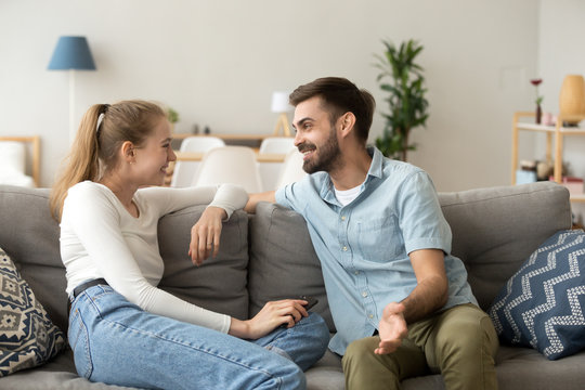 Affectionate cheerful married couple in love or friends spend free time together on weekend talking laughing communicating sitting in living room at home. Dating and not boring with each other concept