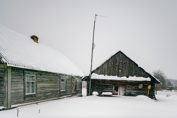 Beautiful wooden house covered with fresh fallen snow.  Uninhabited old winter cozy cottage in empty village. Rural wintertime snowy landscape with forest on background. Scenic countryside view.