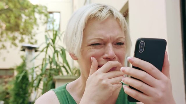 A pretty young blonde woman wearing a green dress sitting outside and using a phone. Close-up shot