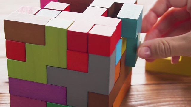 Hand folds colorful wooden cube puzzle on the brown table background, close up. Concept of decision making process, logical thinking. Geometric shapes on a wooden background.