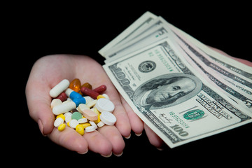 Money and pills in hands, isolated on black. Wasting too much money on medication. Drug addiction...