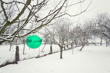 Green Christmas ball vintage glass decoration hanging on tree outdoors, falling snow winter...