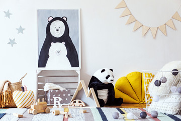 Stylish scandinavian kid room with mock up photo poster frame on the pattern wall, boxes, teddy bear and toys. Cute modern interior of playroom with white walls, wooden accessories and colorful toys.