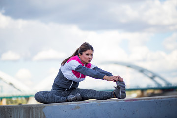 Active fitness woman doing stretching legs in urban area