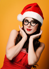 Beautiful brunet girl in christmas hat with glasses on yellow background.