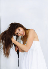 Woman in bathrobe drying her hair with dryer over white background