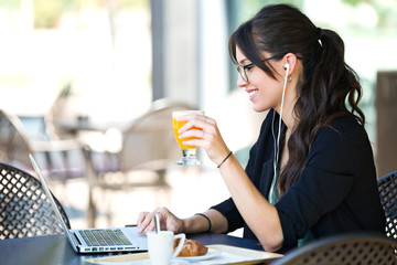Beautiful young woman drinking orange juice while working with her laptop in a coffee shop.