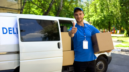 Postal office worker taking parcel box from delivery van and showing thumbs up
