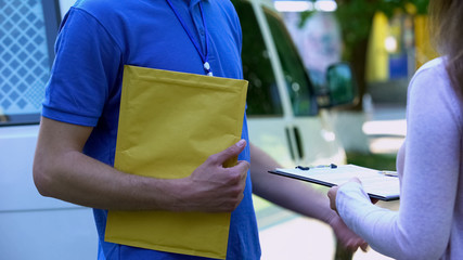 Woman signing proof delivery form and receiving yellow package from courier