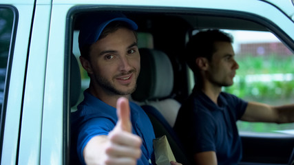 Fototapeta na wymiar Young delivery man holding parcel, showing thumbs up in van, express shipment