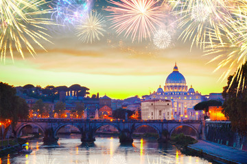 Fototapeta na wymiar illuminated St. Peter's cathedral over bridge and river in Rome at sunset with fireworks, Italy