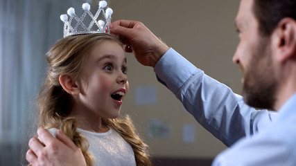 Dad putting princess crown on daughter head, playing game at home, surprise © motortion