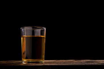 Glass of orange water on wooden table with black background.