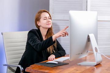 Portrait of happy young successful businesswoman at office. She sits at the table and points to the display. Black Friday or Cyber Monday. Selecting items