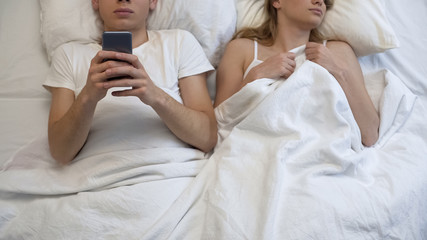 Obraz na płótnie Canvas Boyfriend playing smartphone games in bed, ignoring girlfriend, couple problem