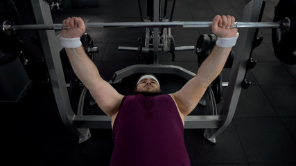 Fototapeta premium Motivated fat man lifting barbell, pumping-up his muscles, healthy lifestyle