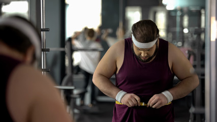 Obese man measuring fat waist, checking result after dieting and training health