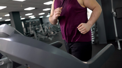 Obese male jogging on treadmill to lose weight, doing cardio exercise in gym