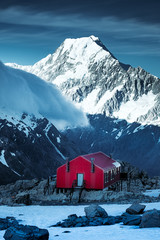 Winter landscape view of red mountain hut and Mt Cook peak, NZ