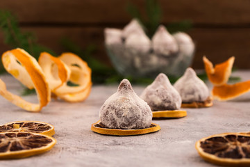 A beautiful dessert for the festive table - chocolate truffles in powdered sugar, slices of dry lemon, branches of spruce on a wooden background.