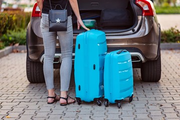 Woman putting two blue plastic suitcases to car trunk.