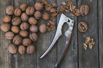 Whole and chopped walnuts on wooden table with nut cracker tool