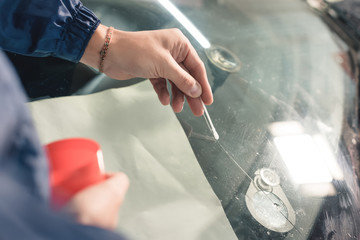 Close up Automobile glazier worker fixing and repair windscreen or windshield of a car in auto service station garage