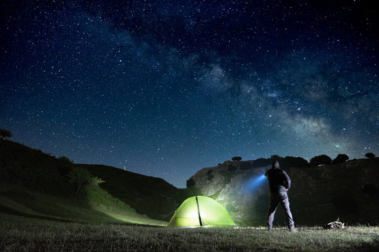 Man Pointing Blue Flashlight To Mountain Below Starry Sky